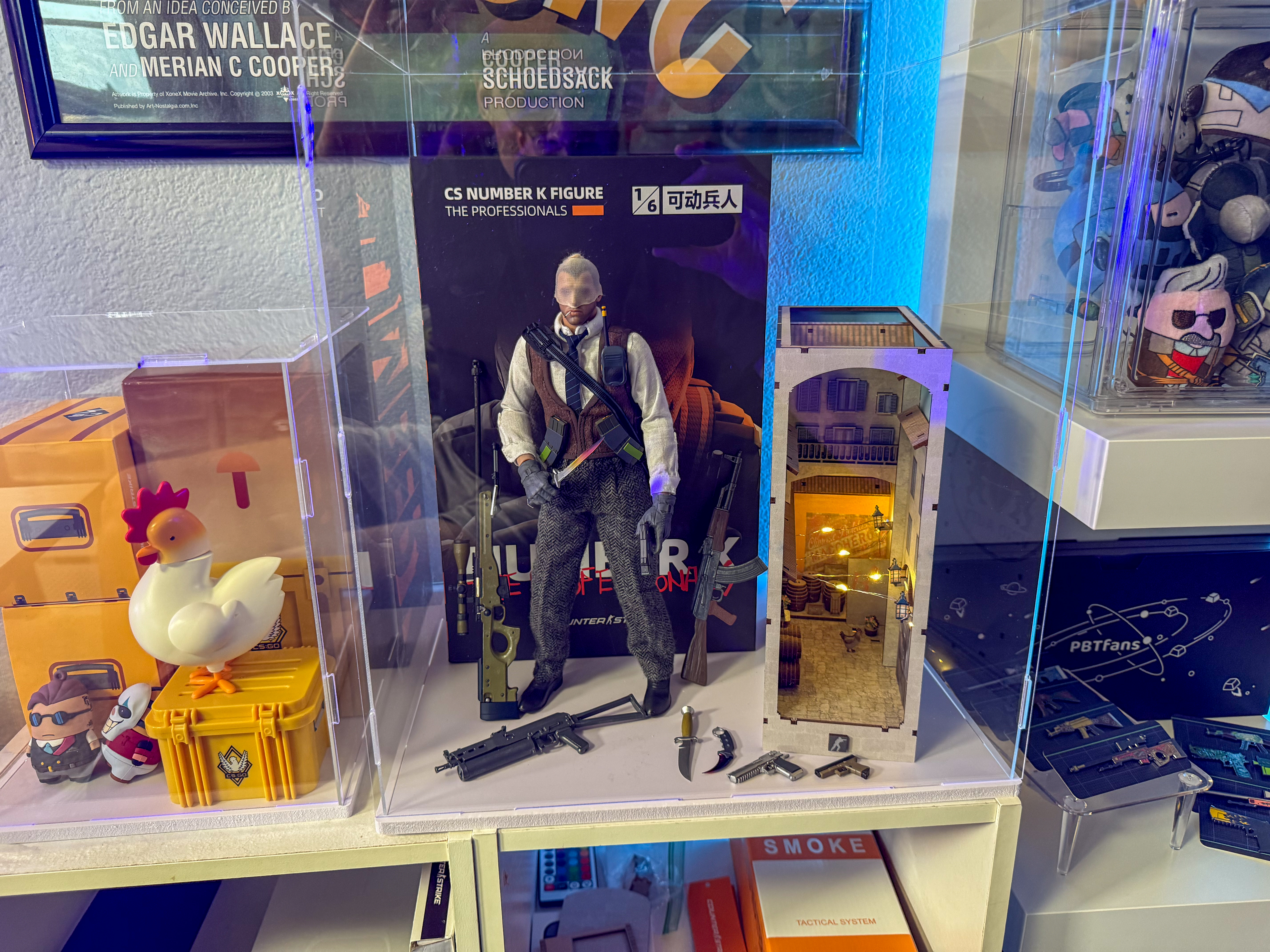 CS2 Agent number K figurine and Inferno bannana bookend on right in acrylic case. CS2 Chicken case, skin pin boxes, and mini figures in acrylic box on the left.